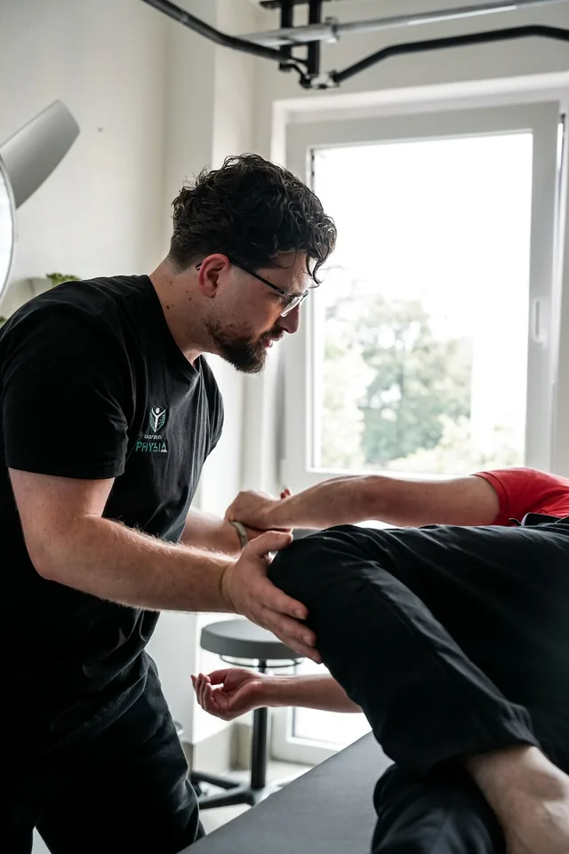 Ein Therapeut bewegt ein Knie an der Behandlungsliege, dahinter ein Fenster