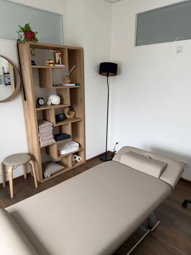 Behandlungsraum mit Liege, Holzregal, rundem Spiegel und Stehlampe