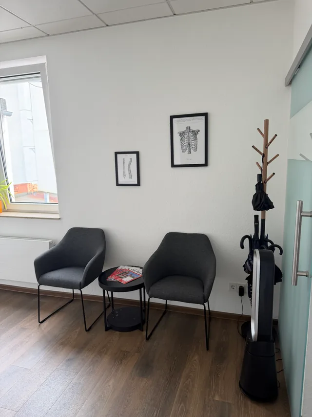 Wartebereich mit zwei Sesseln, Garderobe und gerahmten anatomischen Zeichnungen